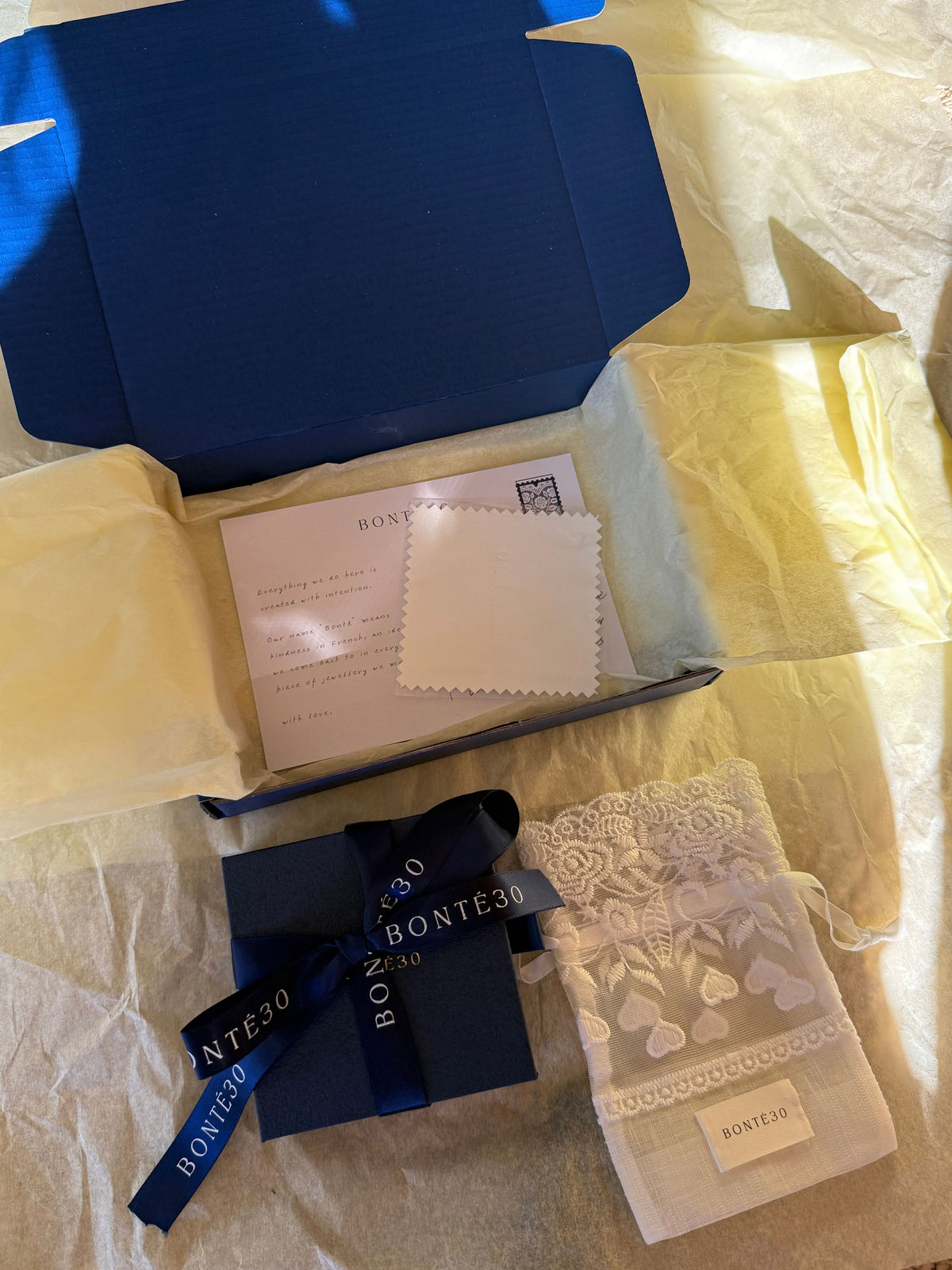 Bonté30 packaging: navy gift box tied with ribbon, lace pouch, polishing cloth and note